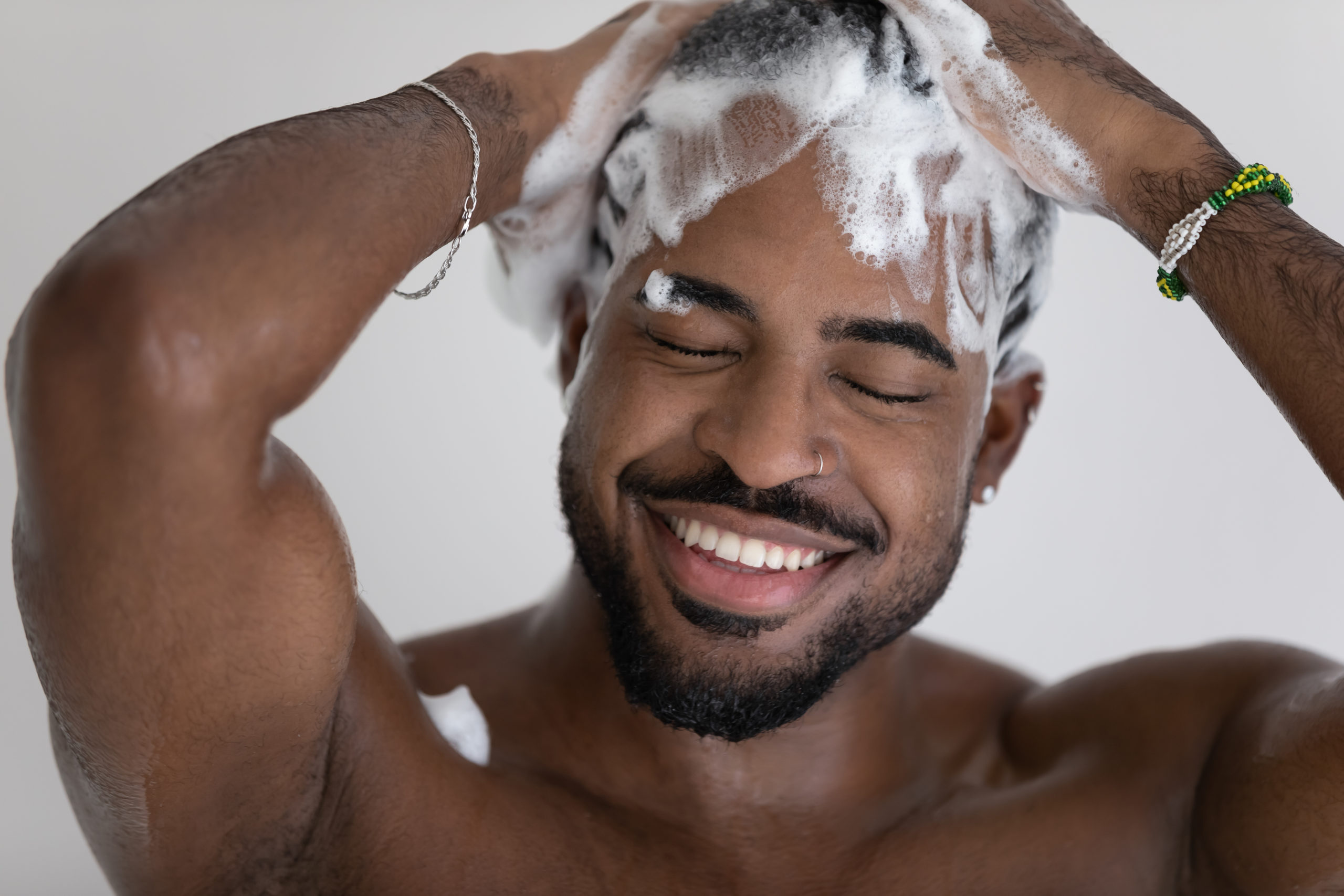 Close up smiling African American man washing hair with shampoo