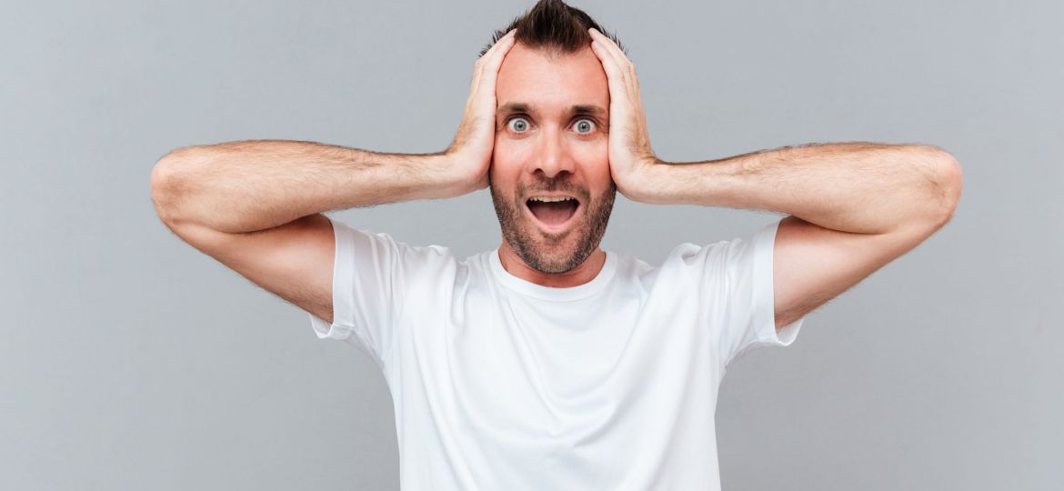 Stressed young man covers ears by hands and shouting