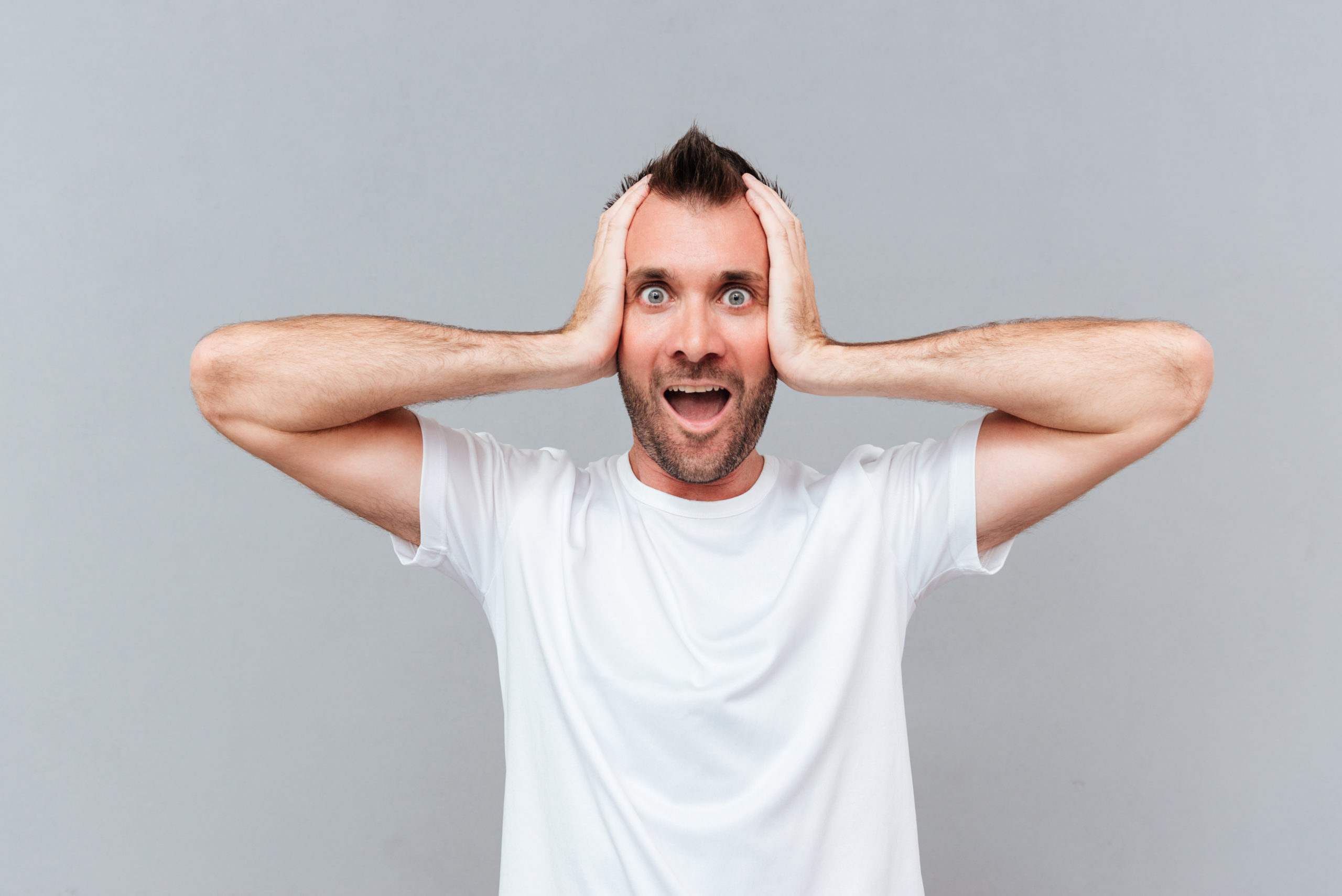 Stressed young man covers ears by hands and shouting