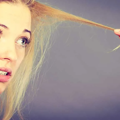 5 Smart Tips to Prevent Split Ends and the Appearance of Thinning Hair - a worried-looking woman with blond hair extends strands of her bangs out in front of her to examine split ends and thinning hair.