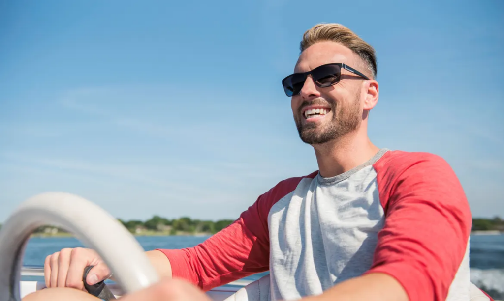 Meet Hair Club Xtrands Client Bret O. - Brett O wearing sunglasses and smiling with hair perfectly in place while driving a boat on a beautiful day.