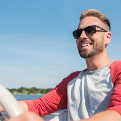 Meet Hair Club Xtrands Client Bret O. - Brett O wearing sunglasses and smiling with hair perfectly in place while driving a boat on a beautiful day.