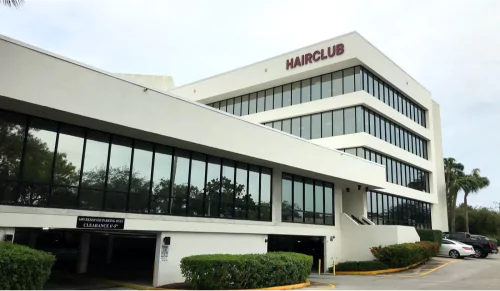 HairClub - About Us - Headquarters - the outside of the HairClub headquarters building - the burgundy HairClub logo is on the top right corner of the white building.