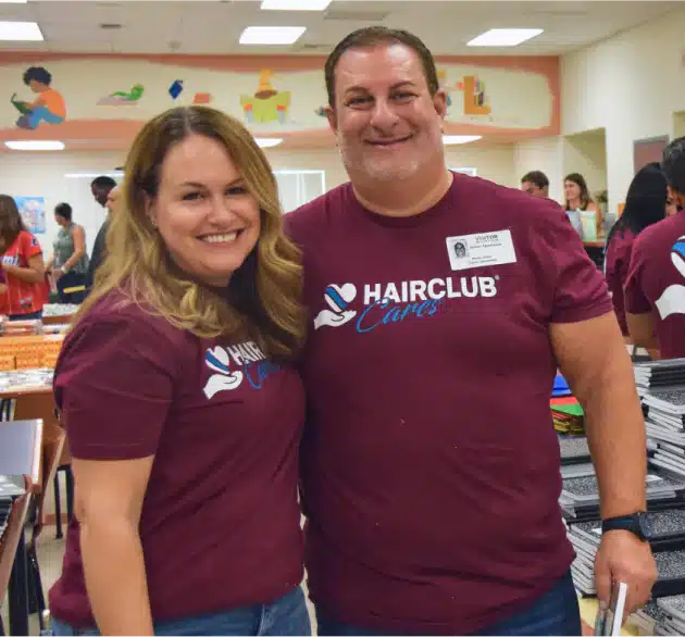 HairClub - What We Believe In - a man and a woman standing close together with an arm around each other's back, smiling at the camera - they are wearing burgundy HairClub Cares t-shirts.