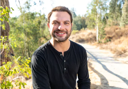 HairClub FUE Long Lasting Solution - a man with a beard and a black shirt posing for a picture on a nature trail - his HairClub Follicular Unit Transplant has given him a full head of hair.