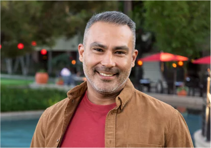 HairClub - FUE - No Scarring - a man standing outside by a pool wearing a red t-shirt underneath an open brown button-down - he has good-looking salt and pepper hair.