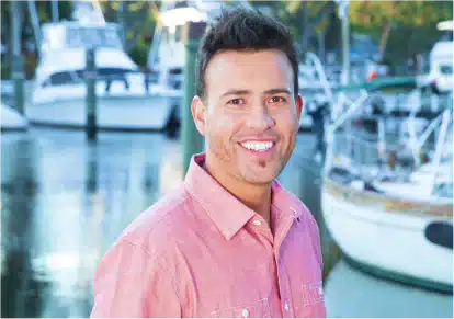 HairClub - Xtrands+ - a guy in a pink dress shirt, standing at a boat dock, looking directly into the camera, showing the successful results of his HairClub Xtrands+ procedure.