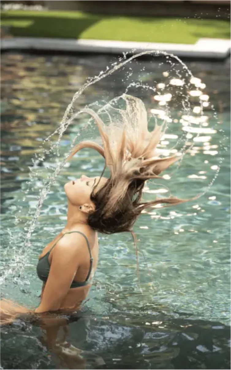 HairClub - Results - a women with long blonde hair in a pool - she is whipping her wet hair back causing water to splatter.