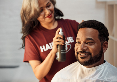 HairClub - Keeps You Looking Good - a man with a nice full head of hair sits in a HairClub Center Salon chair as a HairClub Hair Loss Specialist puts product in his hair.