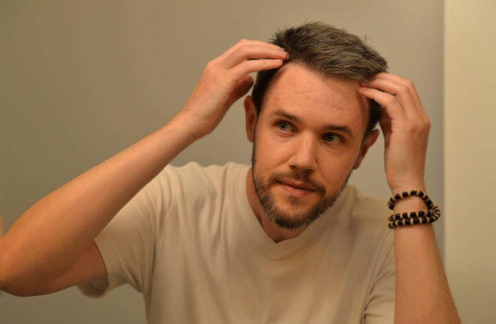 A man examining his thinning hairline in the mirror, illustrating concerns related to which vitamin deficiency causes hair loss.