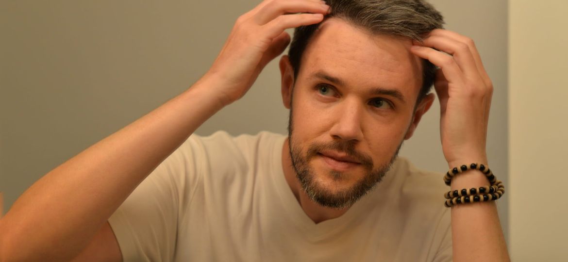A man examining his thinning hairline in the mirror, illustrating concerns related to which vitamin deficiency causes hair loss.