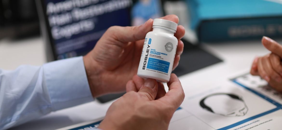 Bosley hair specialist holding DHT blocker supplement bottle during hair loss consultation