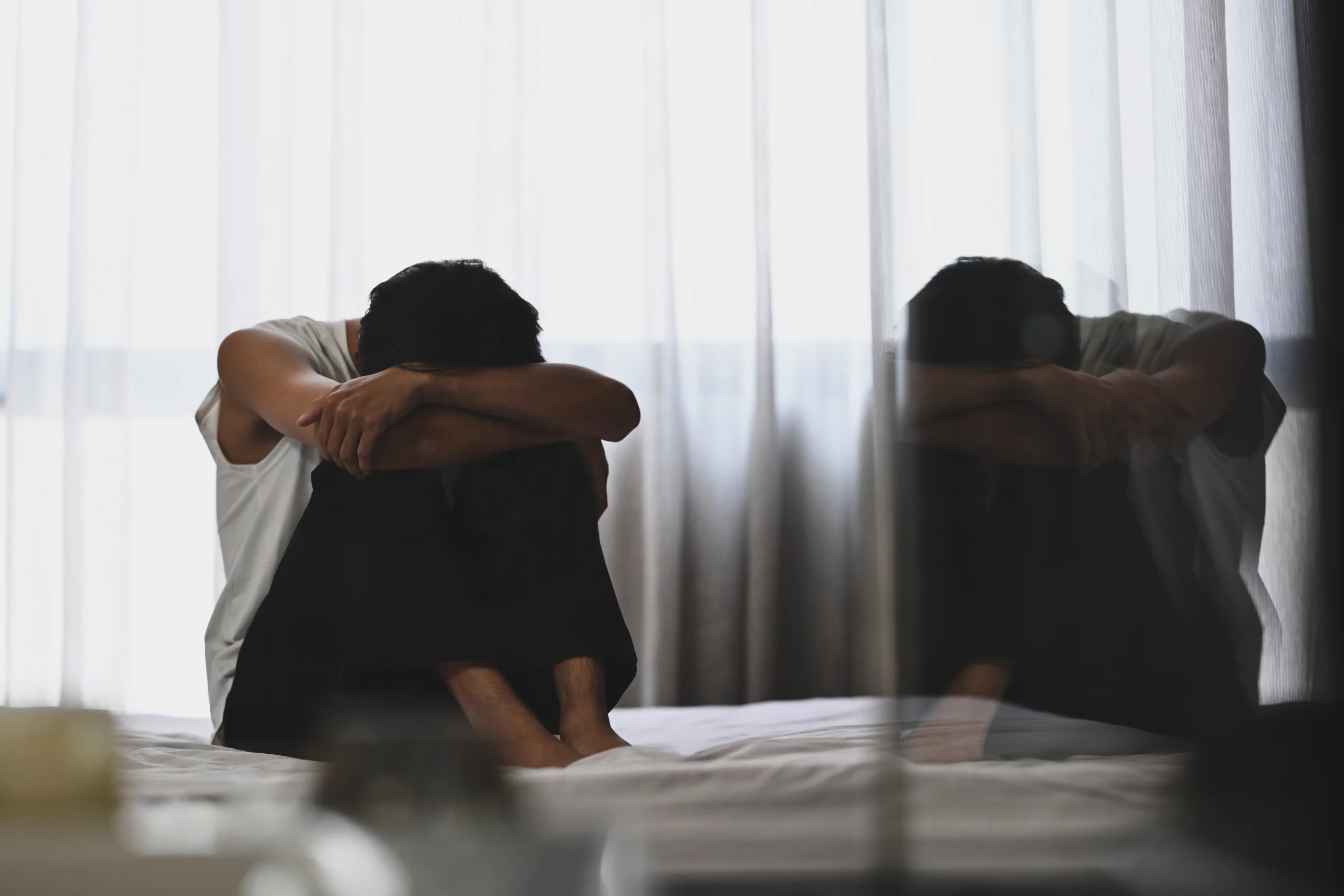 man-sitting-on-bed-with-head-in-hands