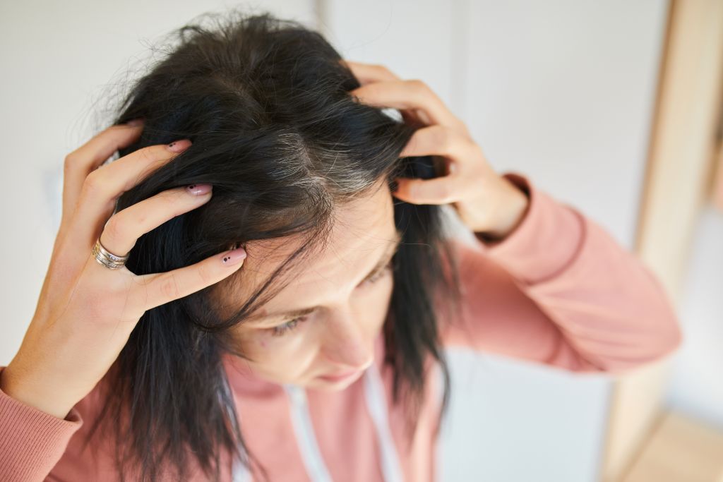 Portrait of a beautiful young woman examining her scalp and hair in front of the mirror,